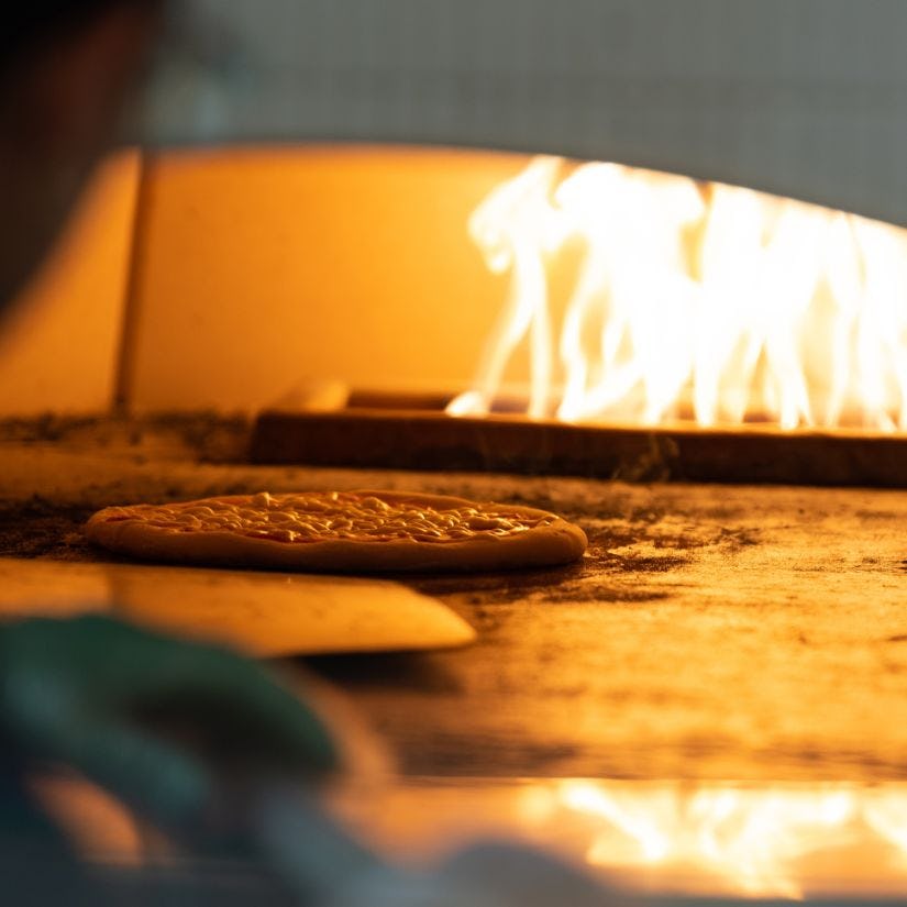 Chef places pizza in flaming hot oven.