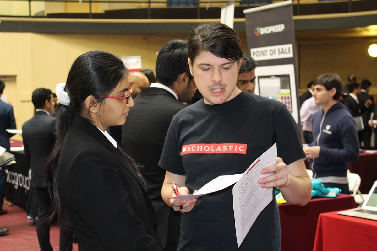 A female student on the left is listening while a male recruiter from Scholastic, standing on the right, goes over her resume