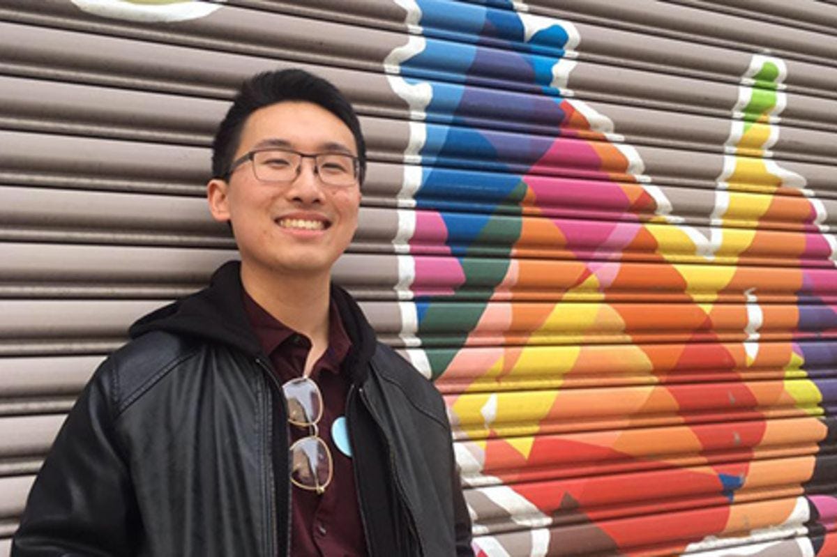 Christopher Liu standing beside some graffiti art in New York City.