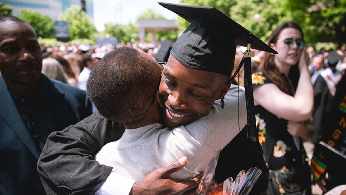 A young man in graduation regalia embraces his mother at commencement.