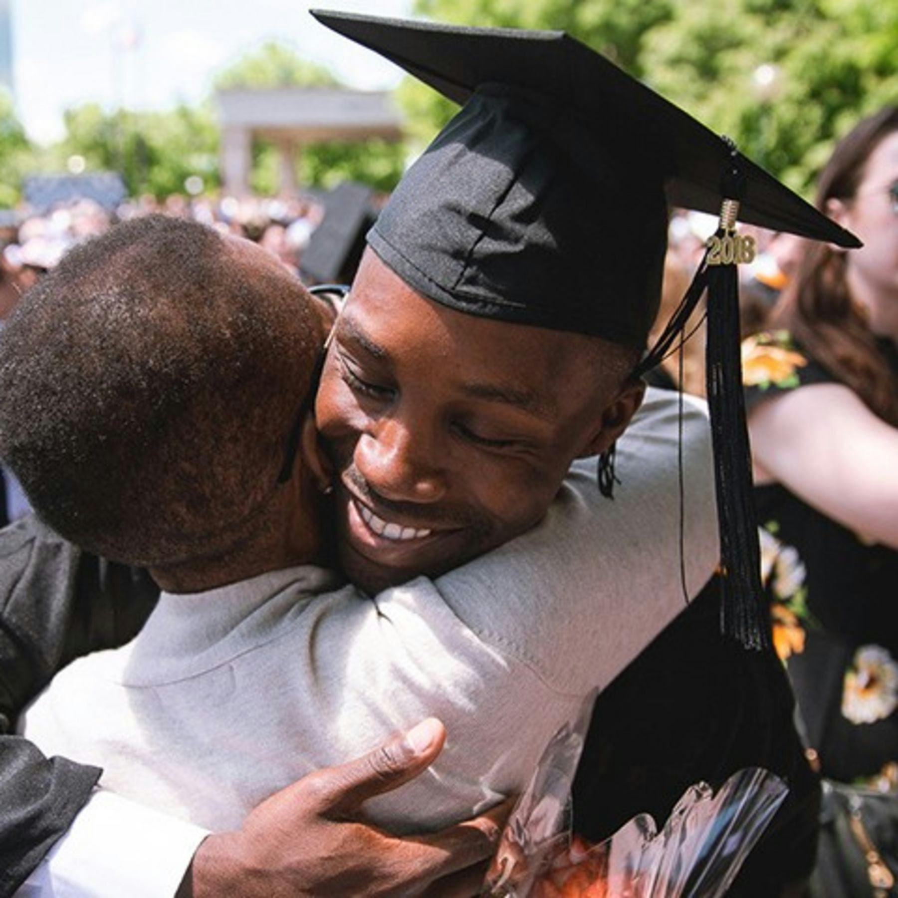 A young man in graduation regalia embraces his mother at commencement.