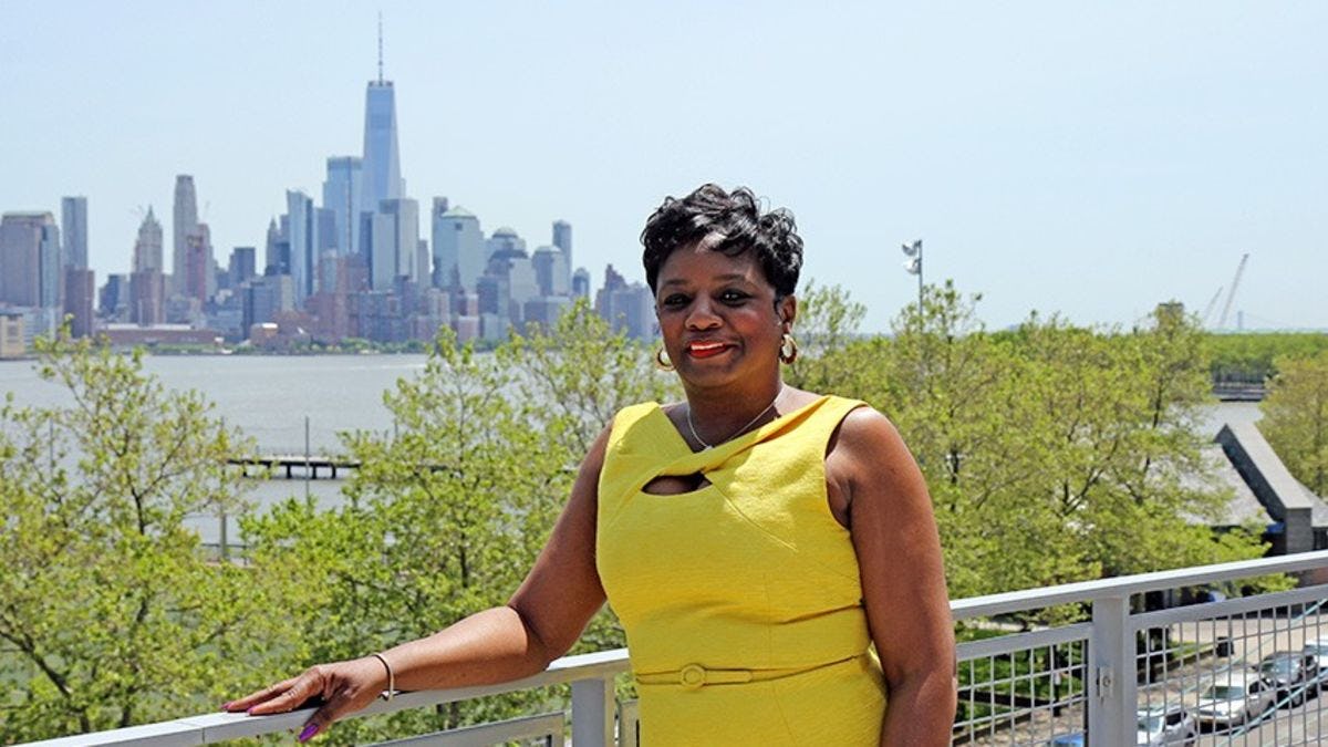 Pam Charleston in a yellow dress with downtown Manhattan in the background.