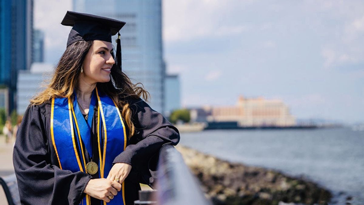 Fatine Zaaj, in cap and gown, on the Hudson River in Jersey City.