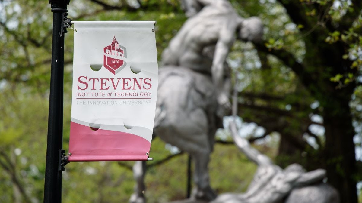 Stevens logo flag in front with torch bearer statue in background