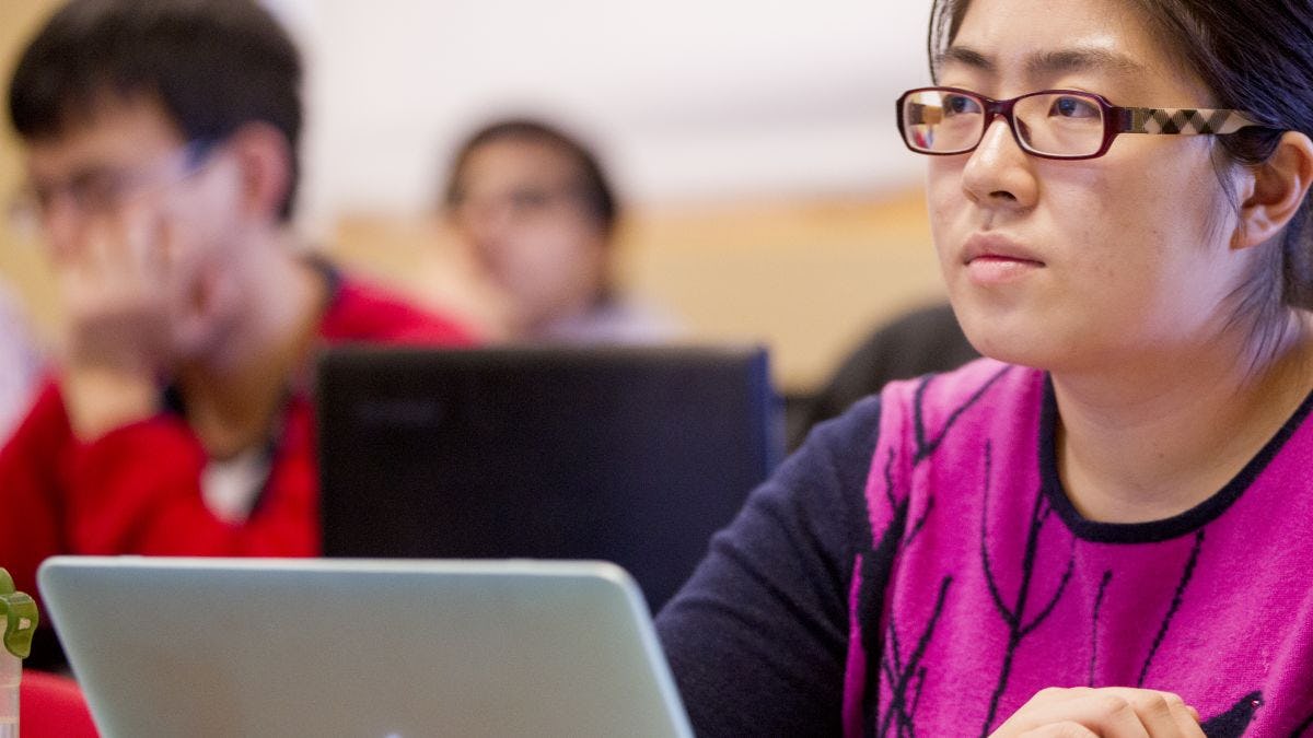 A student with her laptop looks ahead toward lecturing professor