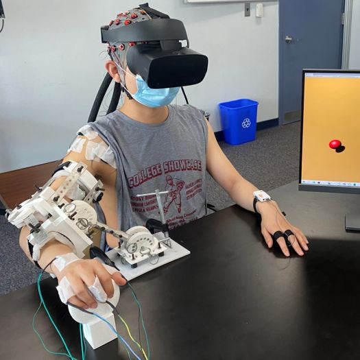 A person wearing a VR headset and arm brace equipped with sensors plays a computer game to improve coordination, strength and muscle control