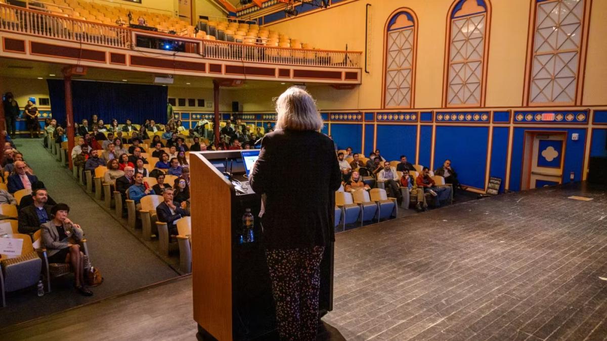 Photo of Manuela Veloso giving a talk behind a podium to an audience in the background