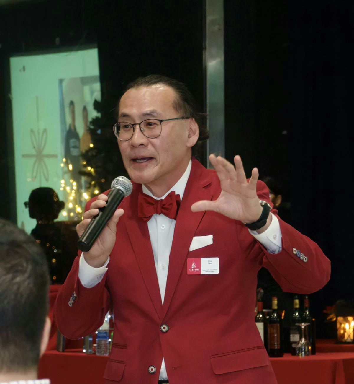 Photo of Woo Lee in a red suit speaking into a microphone